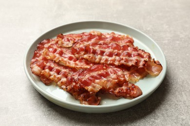 Plate with fried bacon slices on grey textured table, closeup