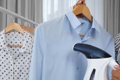 Woman steaming shirt on hanger at home, closeup