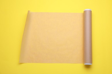 Photo of Roll of baking paper on yellow background, top view