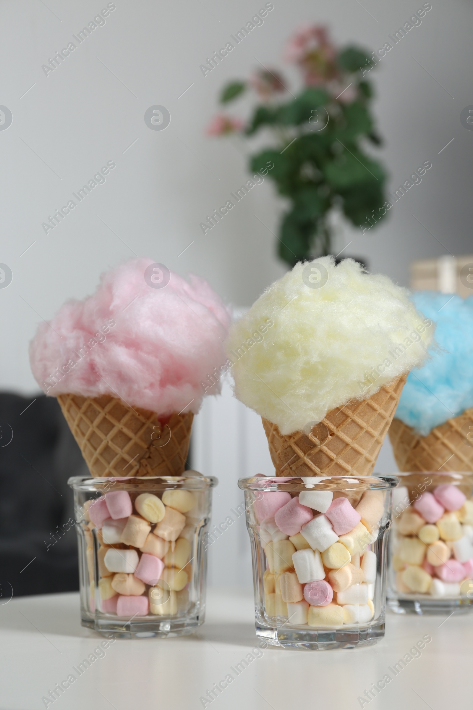 Photo of Sweet cotton candies in waffle cones and marshmallows on white table indoors