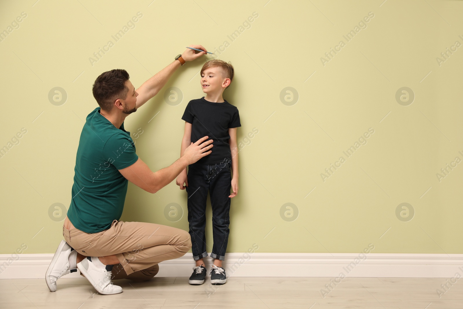 Photo of Father measuring height of his son near light wall indoors. Space for text