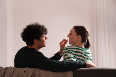 Photo of Boyfriend feeding his girlfriend with popcorn at home. Watching movie
