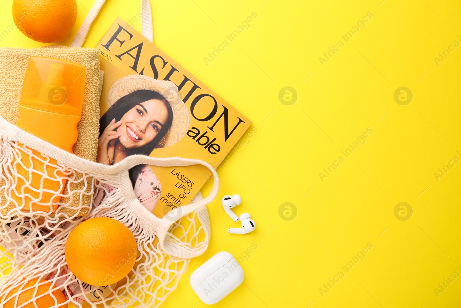 Photo of String bag with fresh oranges, fashion magazine and beach accessories on yellow background, flat lay. Space for text