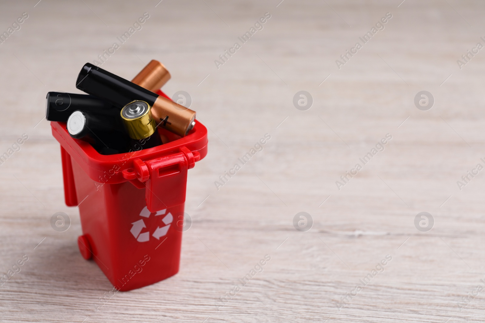 Image of Used batteries in recycling bin on white wooden table, space for text