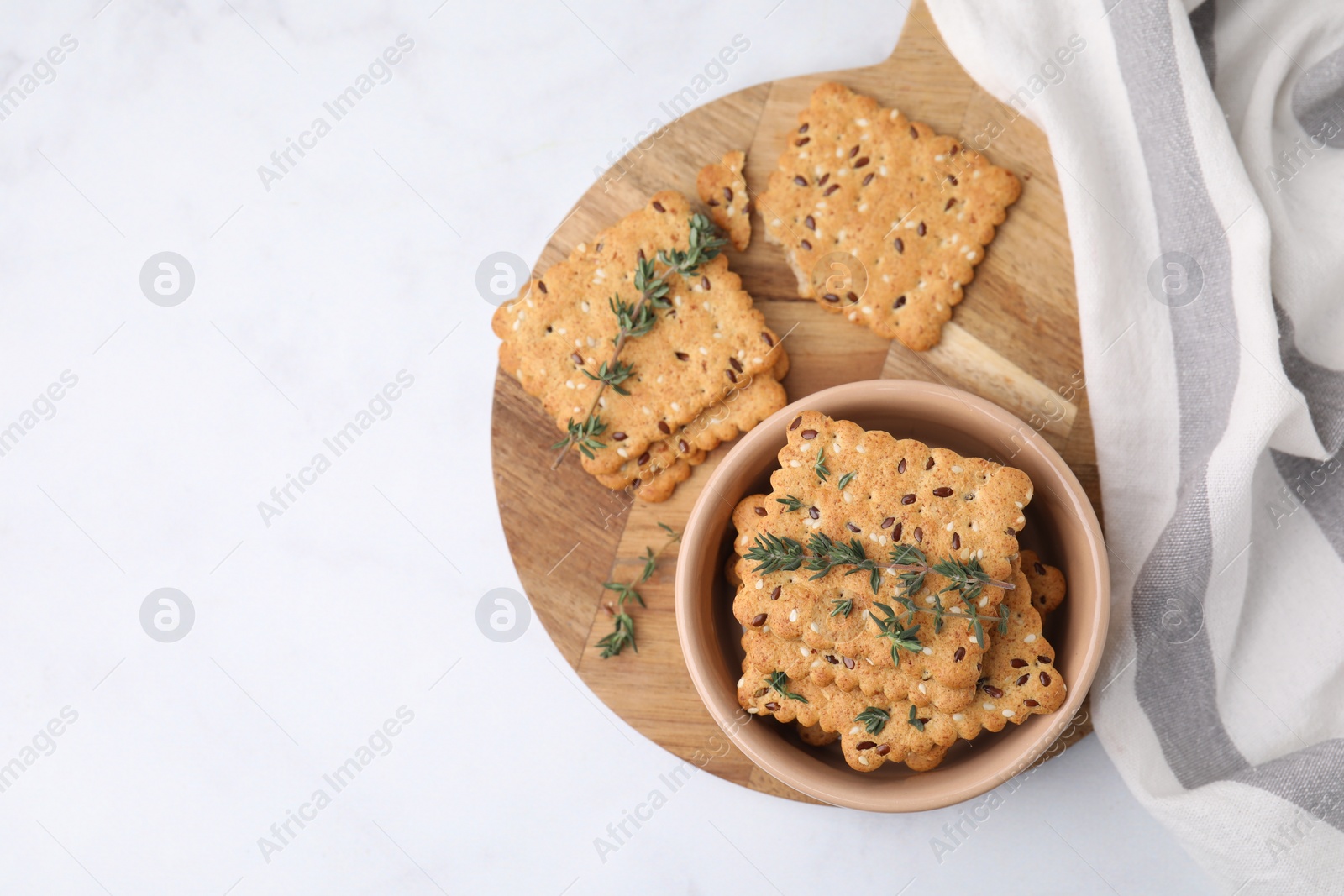 Photo of Cereal crackers with flax, sesame seeds and thyme in bowl on white table, top view. Space for text