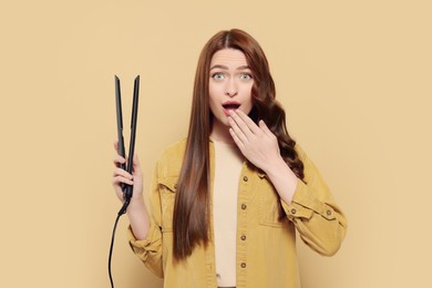 Photo of Emotional woman with hair iron on beige background