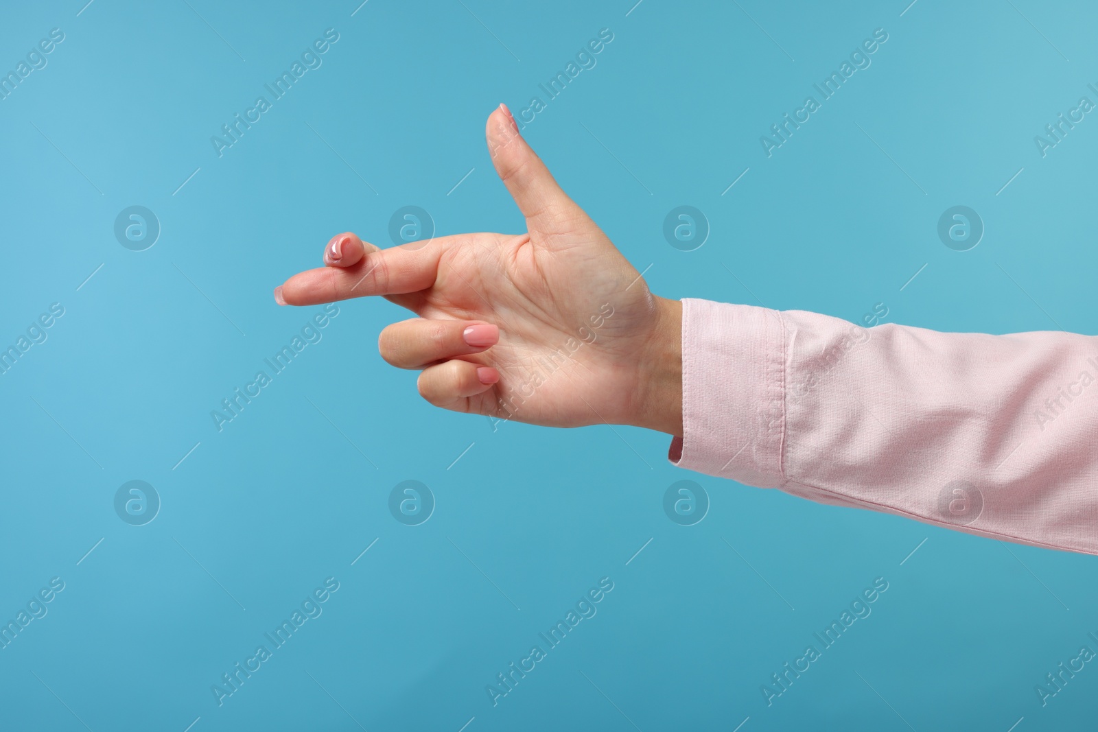 Photo of Woman crossing her fingers on light blue background, closeup