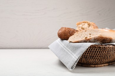 Photo of Different tasty baguettes in basket on white wooden table. Space for text