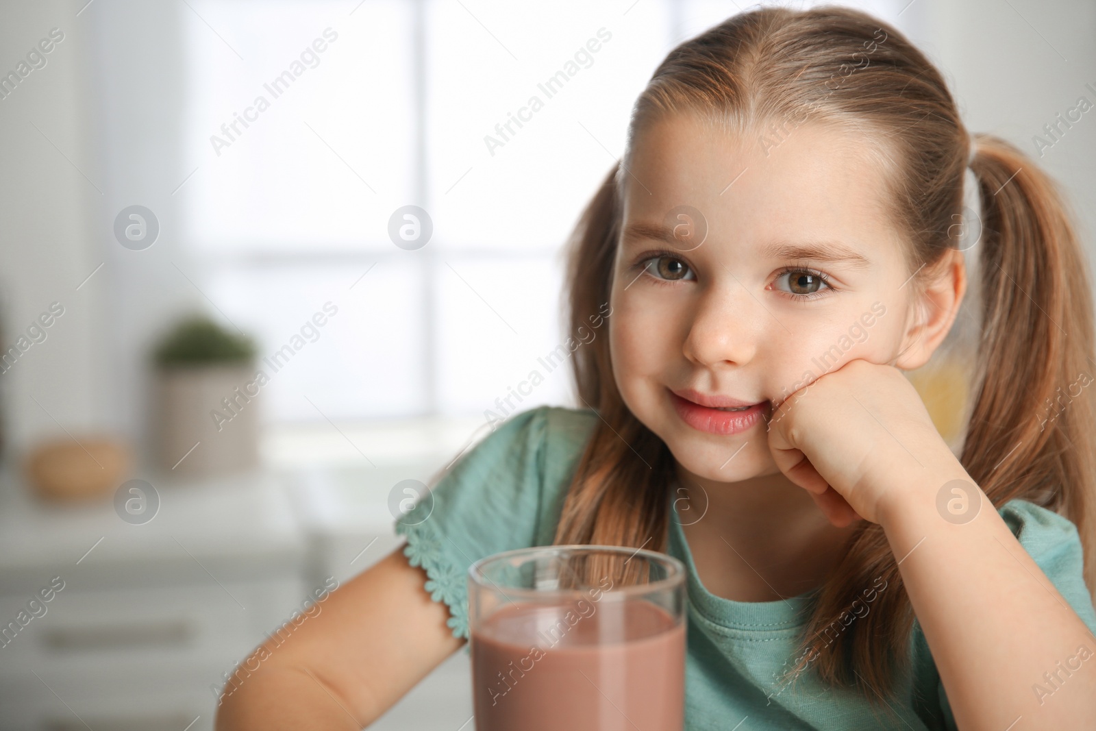 Photo of Cute little child with glass of tasty chocolate milk at home. Space for text