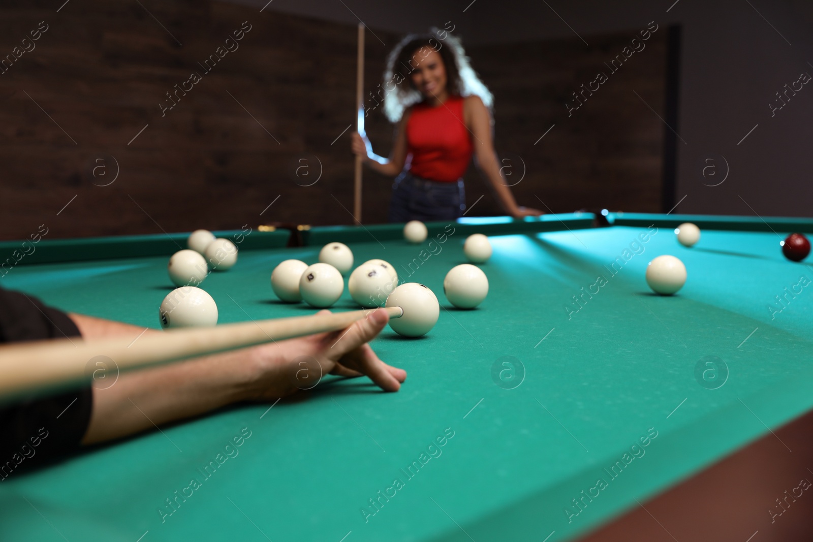 Photo of Young man playing billiard and blurred African-American woman on background, closeup