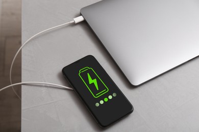 Image of Smartphone with wireless charger connected to laptop on light grey table, above view