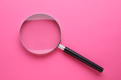 Magnifying glass on pink background, top view