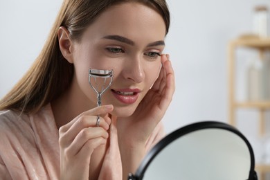 Woman with eyelash curler near mirror indoors