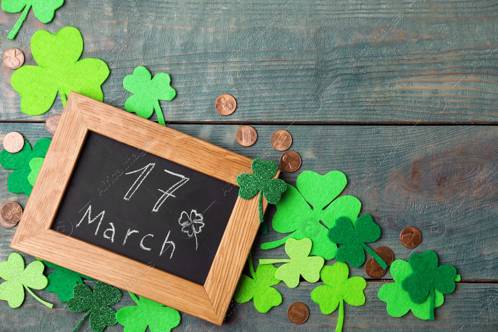 Photo of Chalkboard with written 17 March, clover leaves and gold coins on blue wooden background. St. Patrick's Day celebration