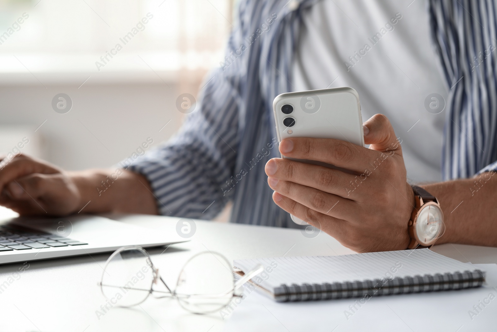 Photo of Man using smartphone while working on laptop at table, closeup