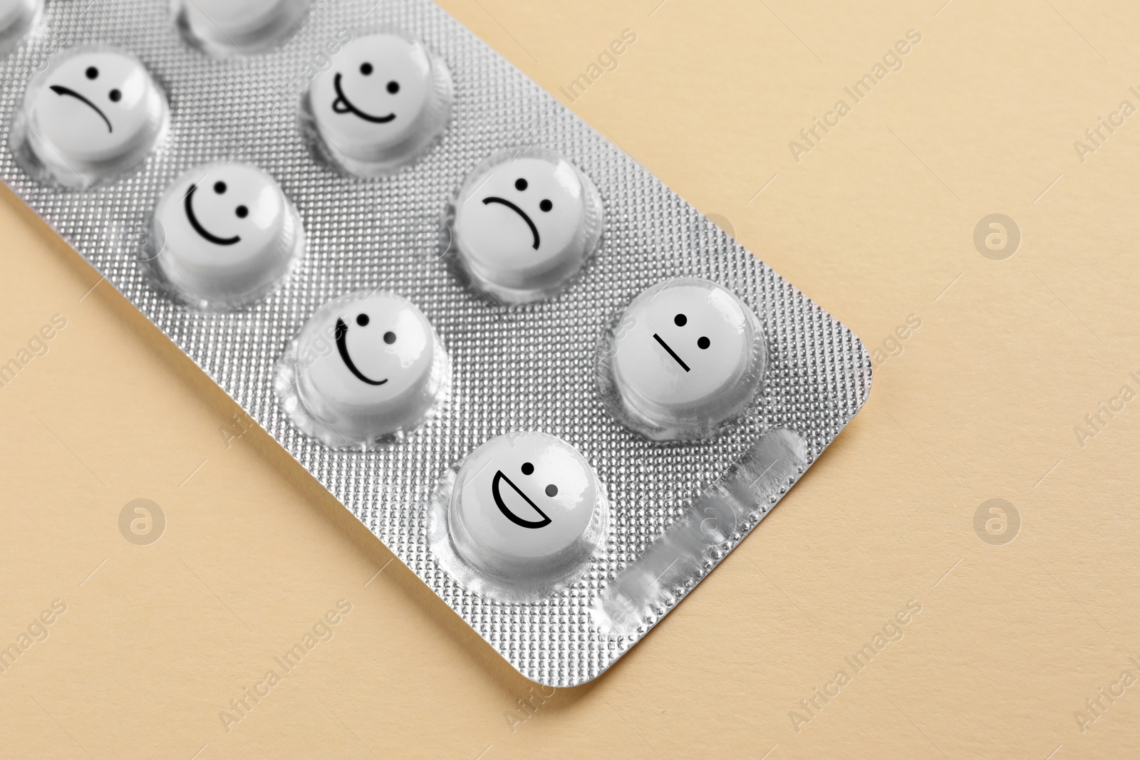 Image of White pills with different emotional faces in blister on beige background