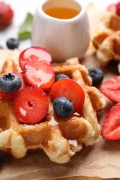 Photo of Delicious Belgian waffle with fresh berries and honey on parchment paper, closeup