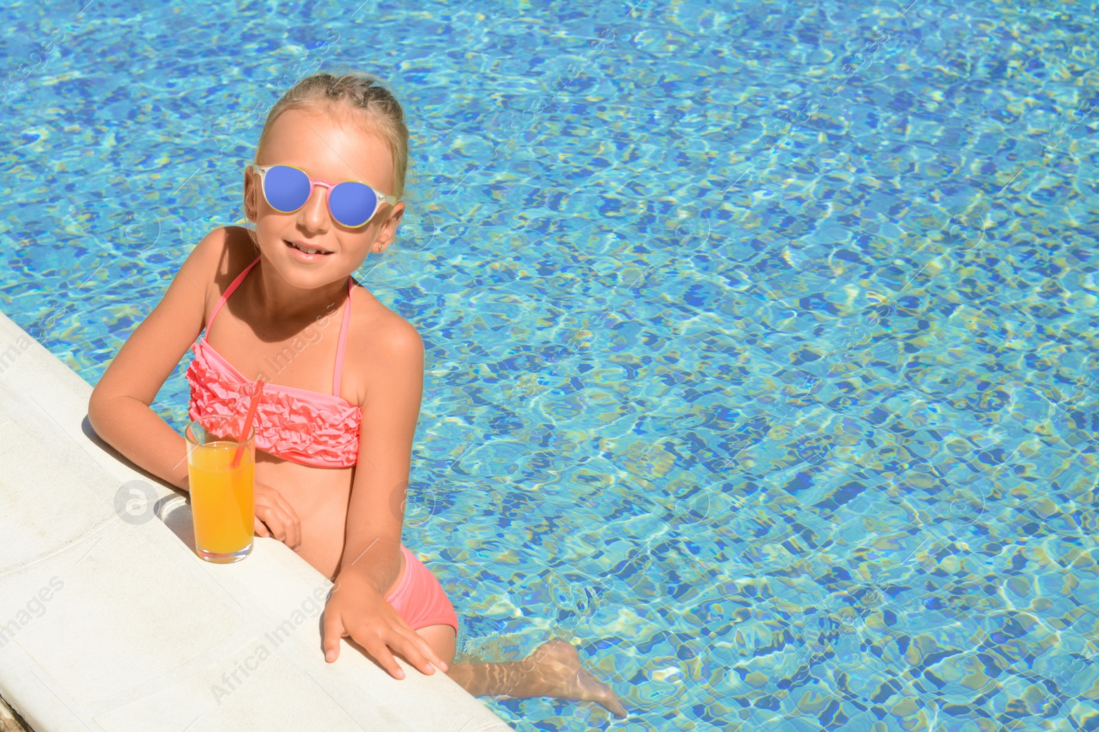 Photo of Cute little girl with glass of juice in swimming pool on sunny day. Space for text