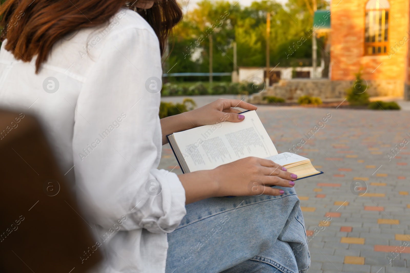 Photo of Young woman reading book outdoors, closeup view