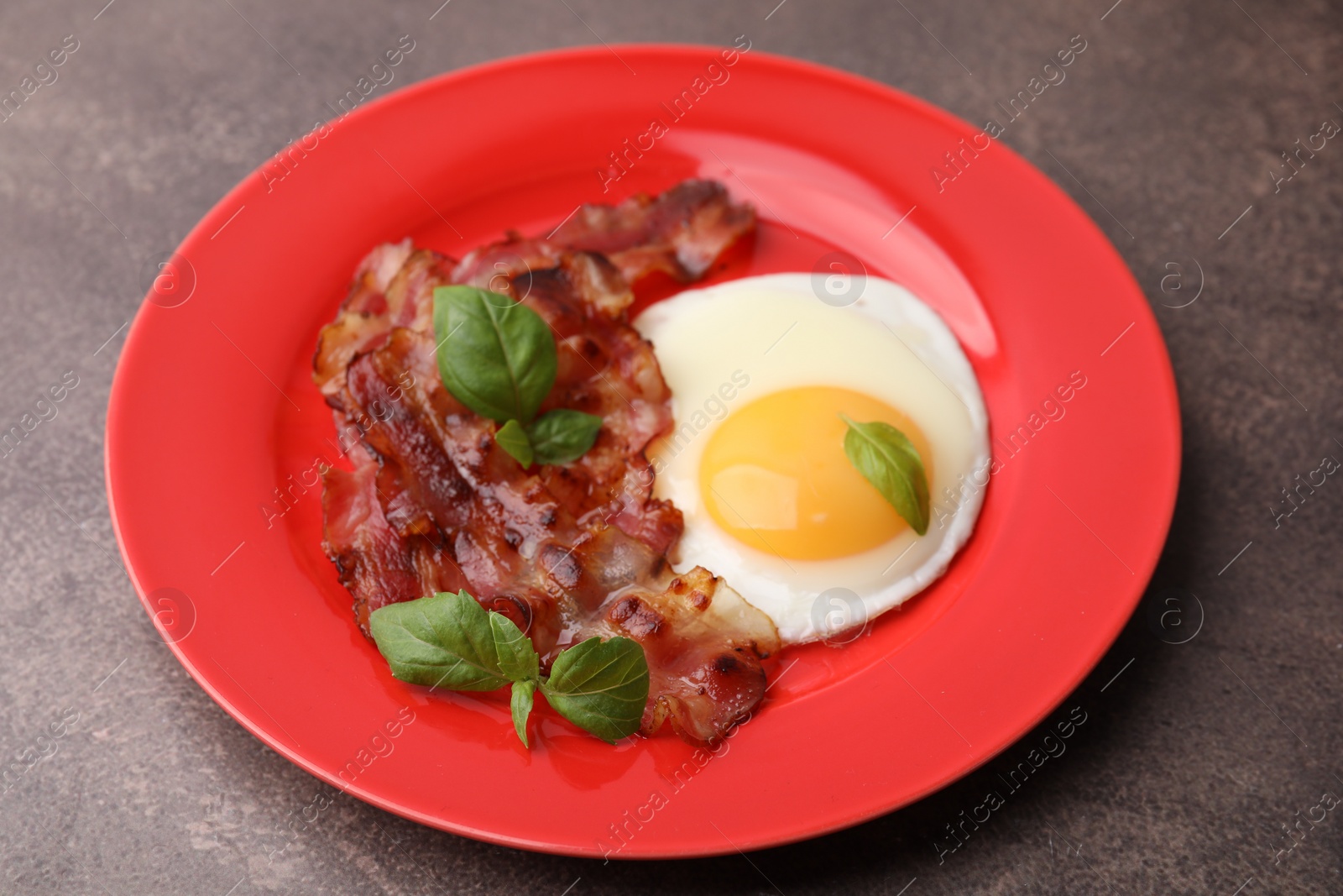 Photo of Fried egg, bacon and basil on brown table