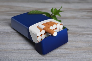Photo of Pack of menthol cigarettes and mint on light wooden table, closeup