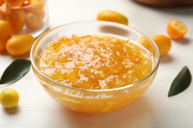 Photo of Delicious kumquat jam in bowl and fresh fruits on white wooden table