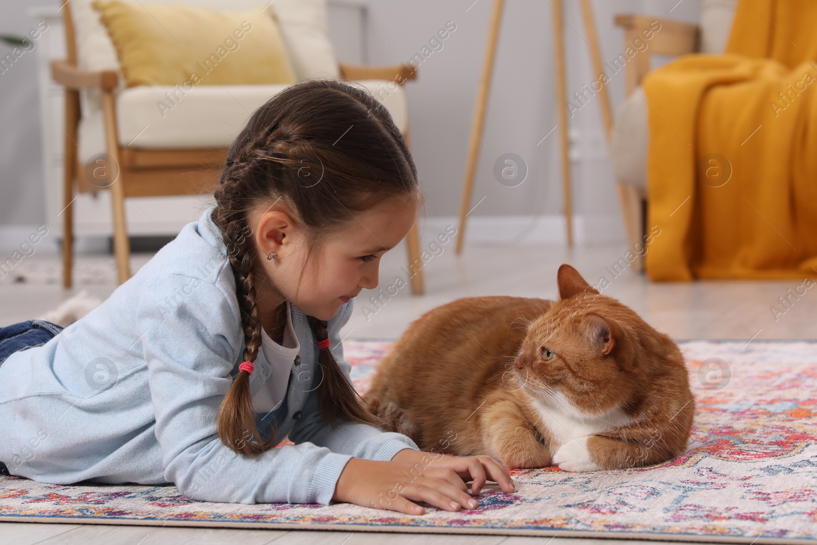 Photo of Little girl and cute ginger cat on carpet at home