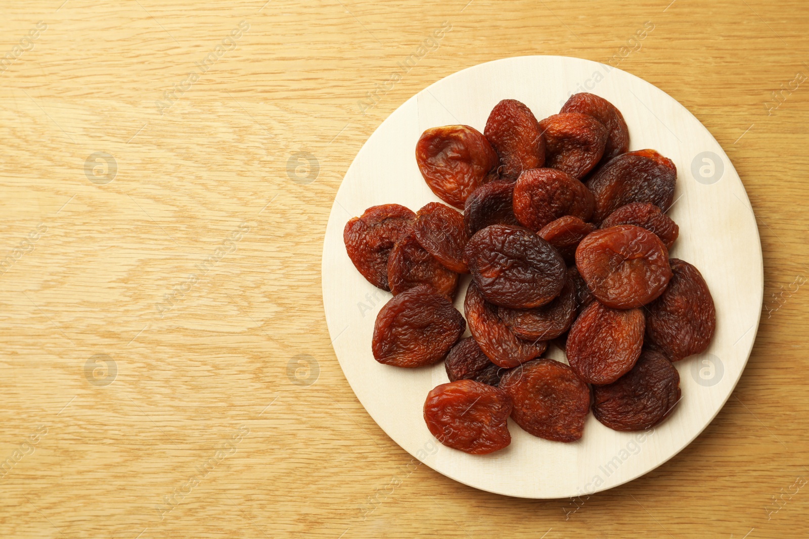Photo of Plate of tasty apricots and space for text on wooden table, top view. Dried fruits