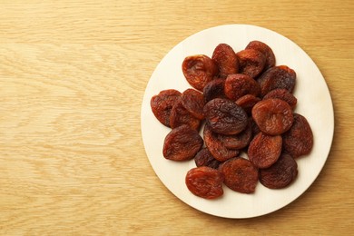 Photo of Plate of tasty apricots and space for text on wooden table, top view. Dried fruits