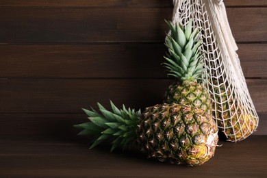 Whole ripe pineapples and net bag on wooden table, space for text