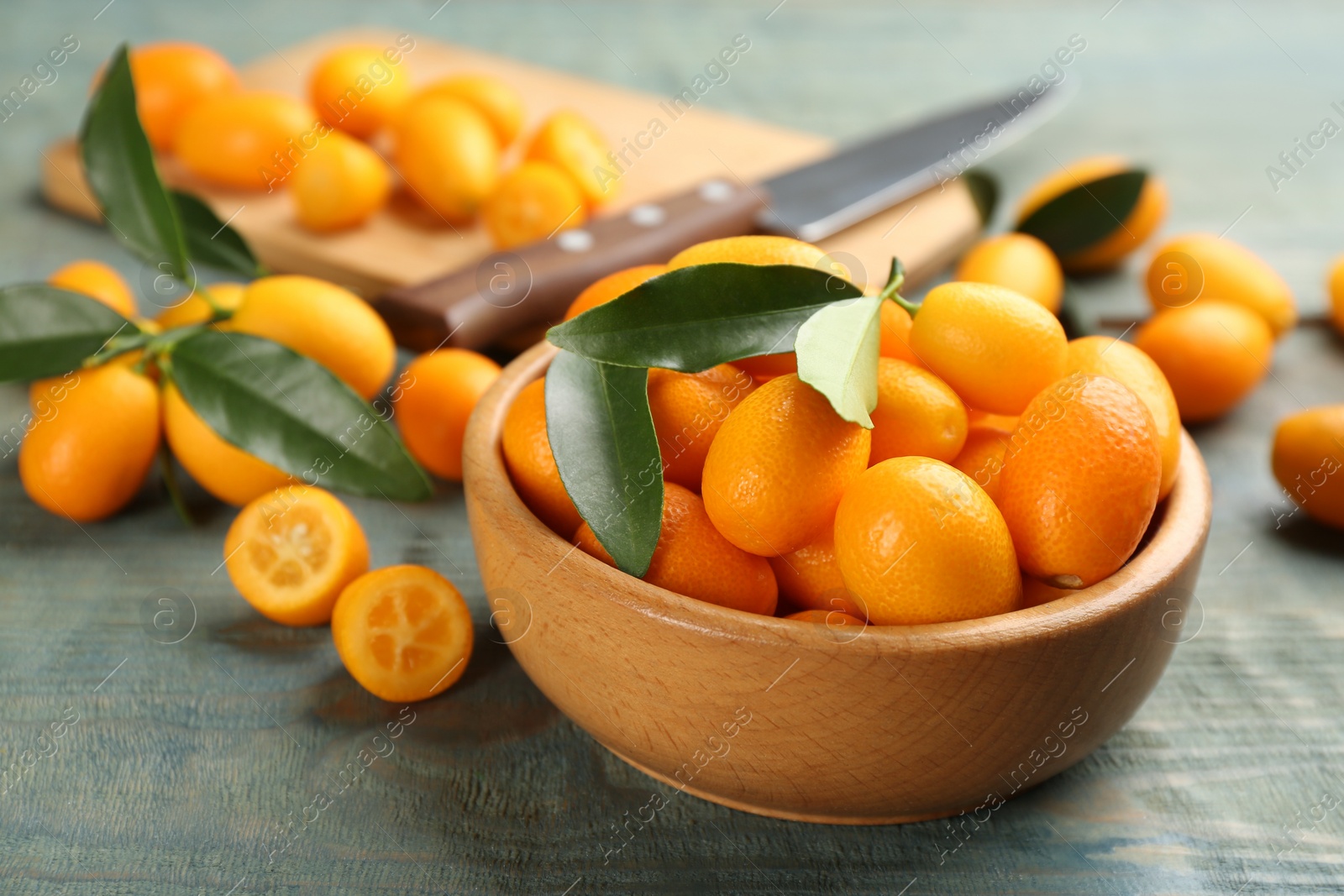 Photo of Fresh ripe kumquats in bowl on light blue wooden table