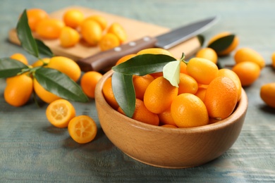 Fresh ripe kumquats in bowl on light blue wooden table