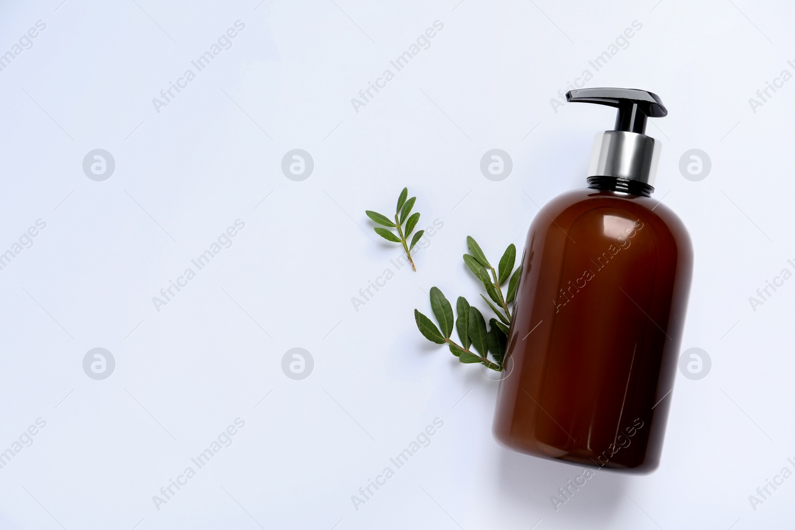 Photo of Bottle of cosmetic product and green leaves on white background, flat lay. Space for text