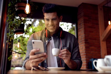 Image of Man using smartphone with facial recognition system in cafe. Security application scanning his face for approving owner's identity