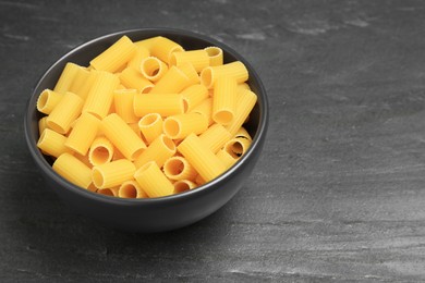 Photo of Raw rigatoni pasta in bowl on grey table, closeup. Space for text