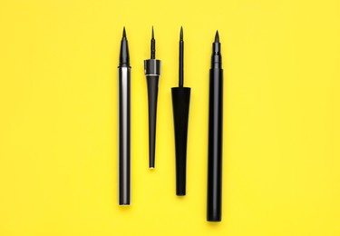 Photo of Black eyeliners on yellow background, flat lay. Makeup product
