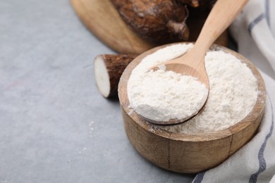 Photo of Wooden bowl and spoon with cassava flour on grey table, closeup. Space for text