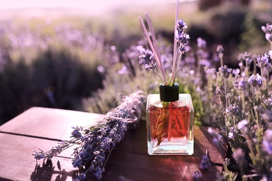 Reed air freshener with oil and fresh lavender flowers on wooden table in blooming field. Space for text