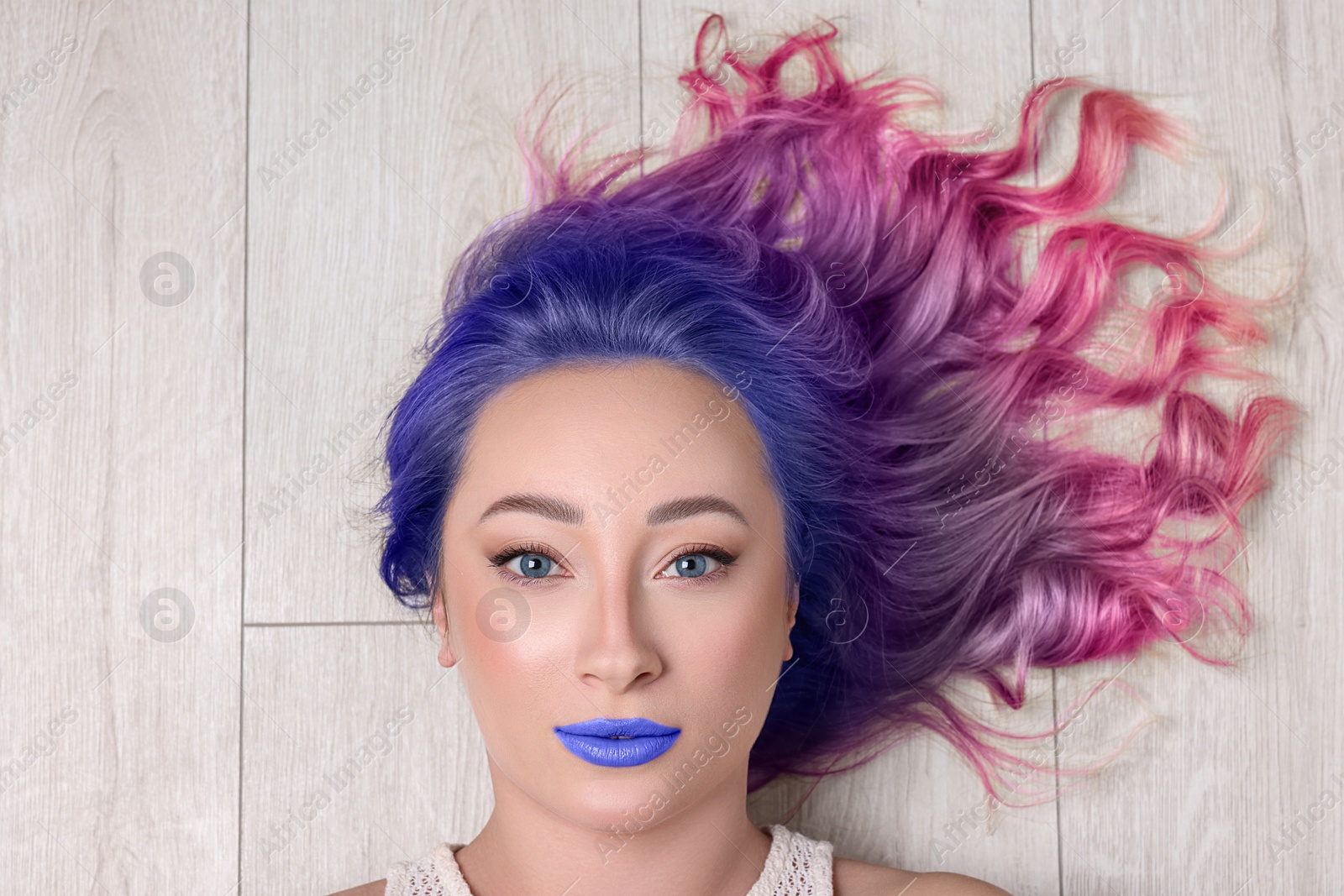 Image of Trendy hairstyle. Young woman with colorful dyed hair on white wooden background, top view