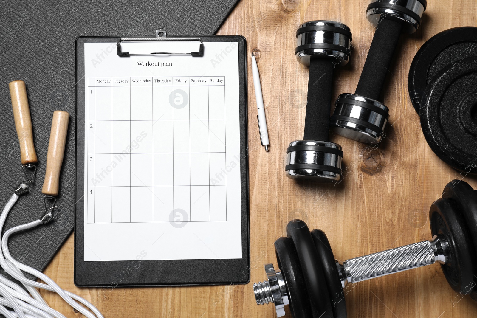 Photo of Clipboard with workout plan and sports equipment on wooden table, flat lay. Personal training