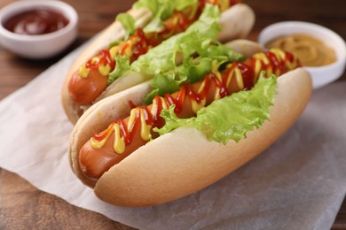 Photo of Tasty hot dogs with lettuce, ketchup and mustard on board, closeup