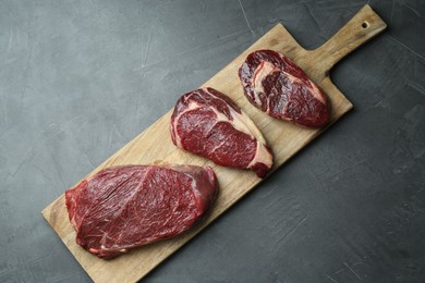 Photo of Wooden board with pieces of raw beef meat on grey table, top view