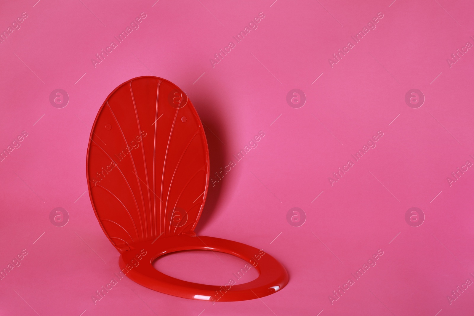 Photo of New red plastic toilet seat on pink background, space for text