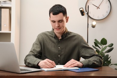 Photo of Man taking notes at wooden table in office