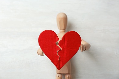 Wooden puppet with torn cardboard heart on gray background. Relationship problems