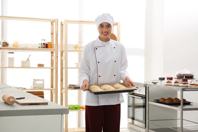 Photo of Female pastry chef holding baking sheet with uncooked croissants in kitchen