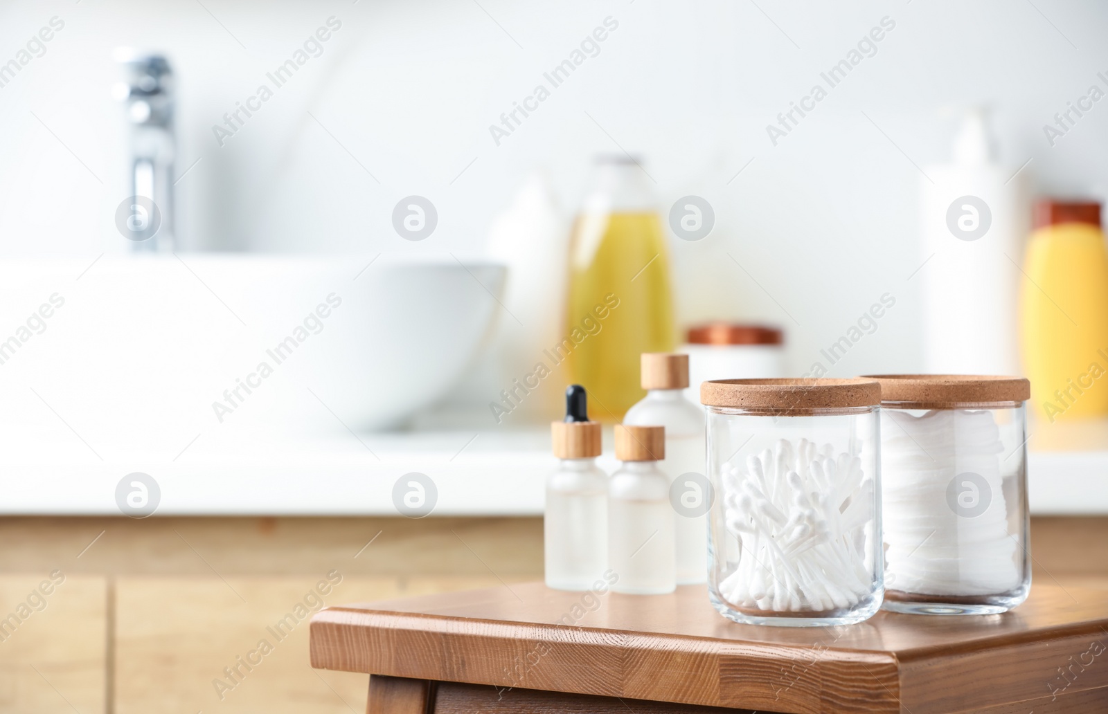 Photo of Cotton pads and swabs near cosmetic products on wooden stool in bathroom. Space for text