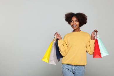 Happy African American woman with shopping bags on light grey background. Space for text