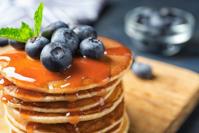 Photo of Wooden board with pancakes, syrup and blueberries on table, closeup