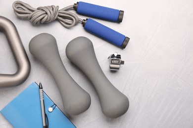Photo of Dumbbells, skipping rope, stationery and timer on light grey table, flat lay. Space for text